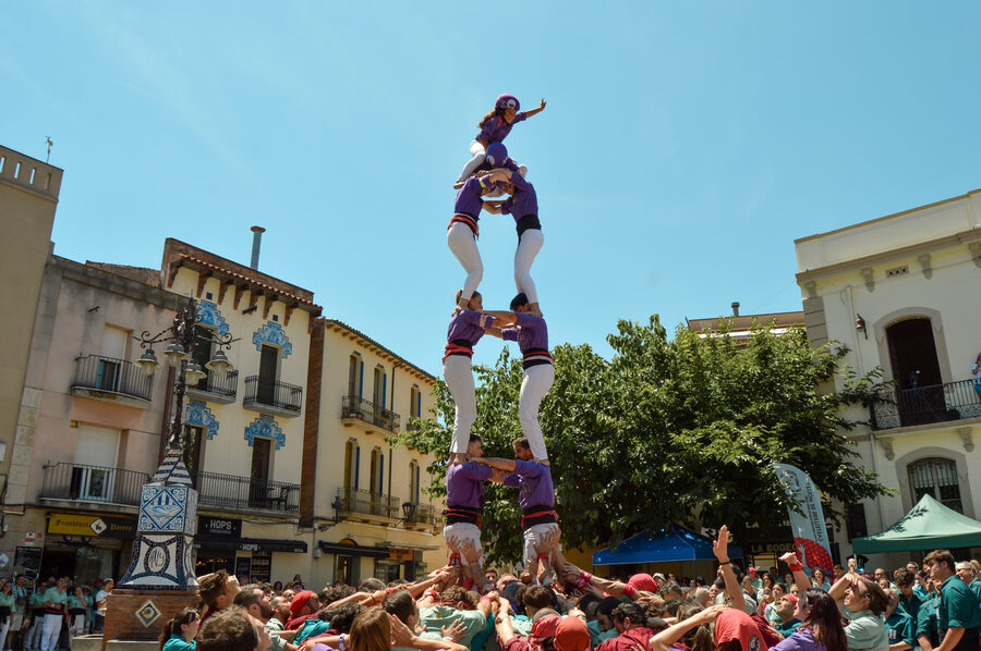 Enxaneta coronando una torre humana con la mano levantada sobre una plaza llena