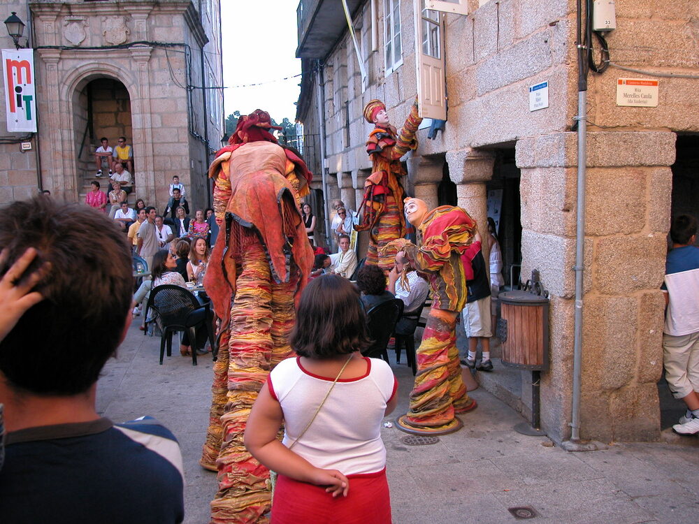 Actores en zancos con trajes de colores actuando en una calle estrecha ante el público