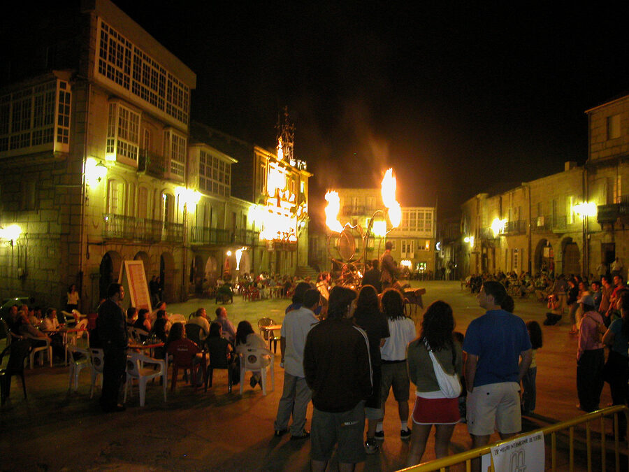 Espectáculo nocturno con llamas en una plaza porticada rodeada de público