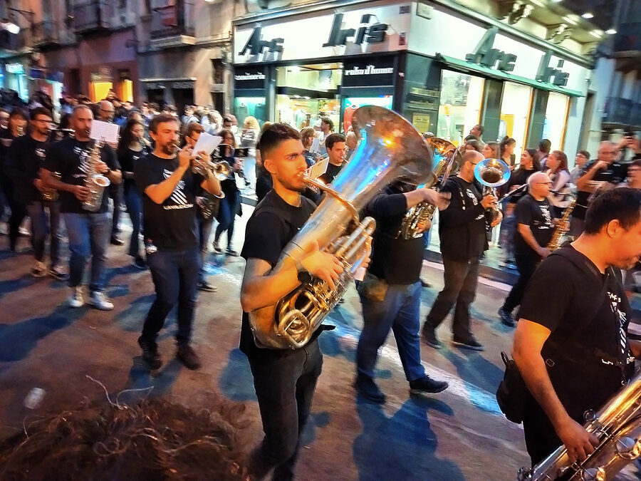 Banda de música desfilando de noche por una calle con tubas, saxofones y trompetas