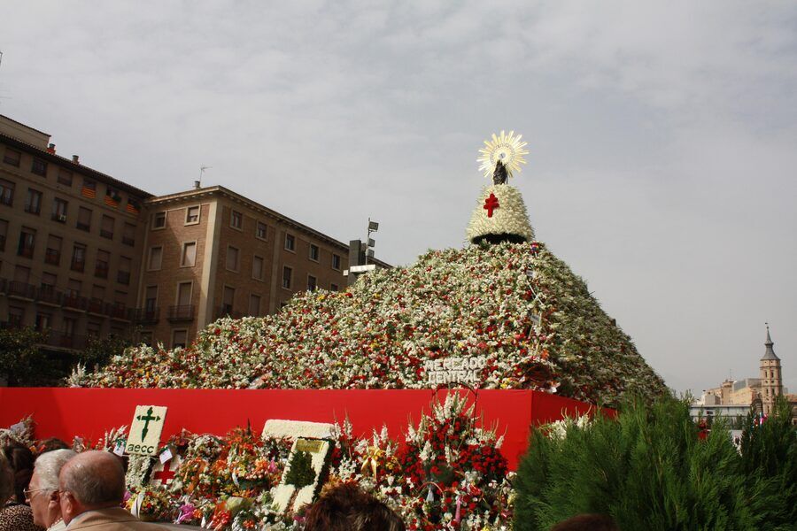 Gran estructura cónica cubierta de flores blancas y rojas con una imagen en lo alto, en una plaza