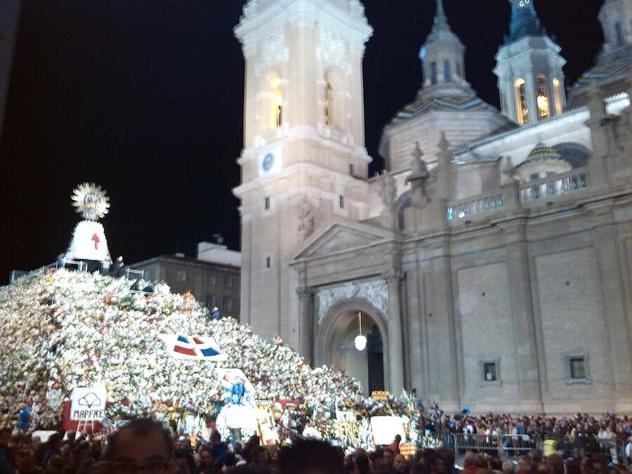 La misma estructura floral ya terminada, iluminada de noche, con el público agolpado alrededor